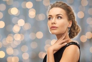 people, holidays and glamour concept - beautiful woman wearing earrings over lights background